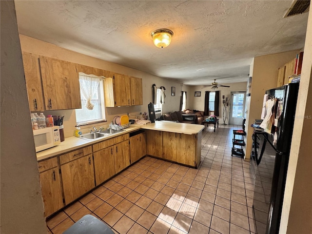 kitchen with white microwave, a peninsula, a sink, freestanding refrigerator, and open floor plan