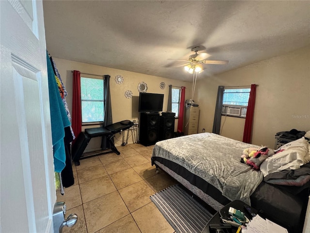 bedroom featuring multiple windows, light tile patterned floors, a ceiling fan, cooling unit, and a textured ceiling