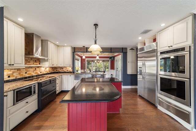 kitchen with built in appliances, wall chimney exhaust hood, a warming drawer, dark wood-style floors, and decorative backsplash