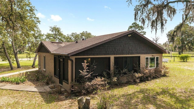 view of home's exterior featuring a yard, stucco siding, a sunroom, and roof with shingles
