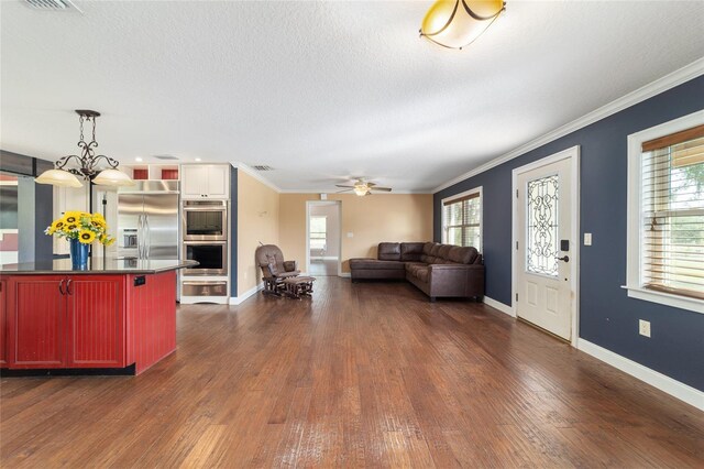 living area featuring dark wood-style flooring, a ceiling fan, baseboards, ornamental molding, and a textured ceiling