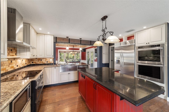 kitchen featuring wall chimney range hood, built in appliances, dark wood-type flooring, a sink, and a textured ceiling