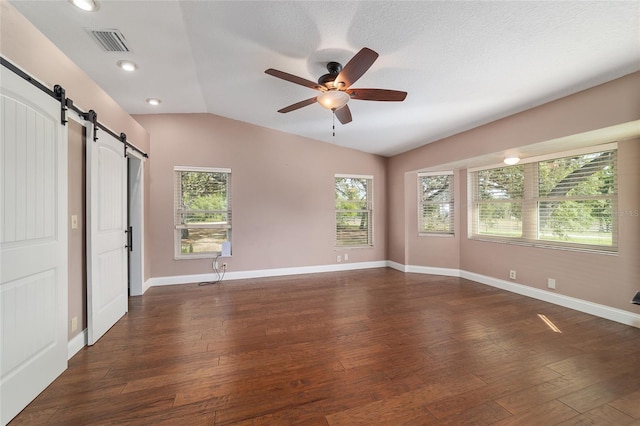 empty room featuring a barn door, vaulted ceiling, a ceiling fan, dark wood-type flooring, and baseboards