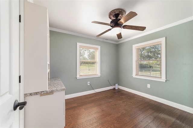 unfurnished room with plenty of natural light, dark wood-style floors, ceiling fan, ornamental molding, and baseboards
