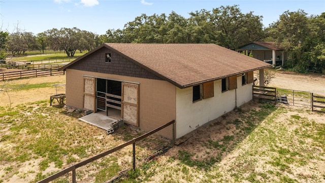 view of side of home with an exterior structure, roof with shingles, concrete block siding, an outbuilding, and view of scattered trees