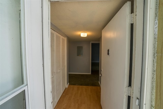 hallway with light wood-style floors, a textured ceiling, electric panel, and baseboards