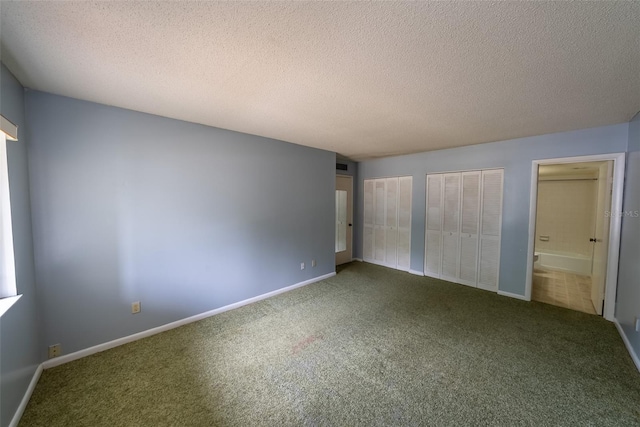 unfurnished bedroom with multiple closets, carpet, a textured ceiling, ensuite bathroom, and baseboards