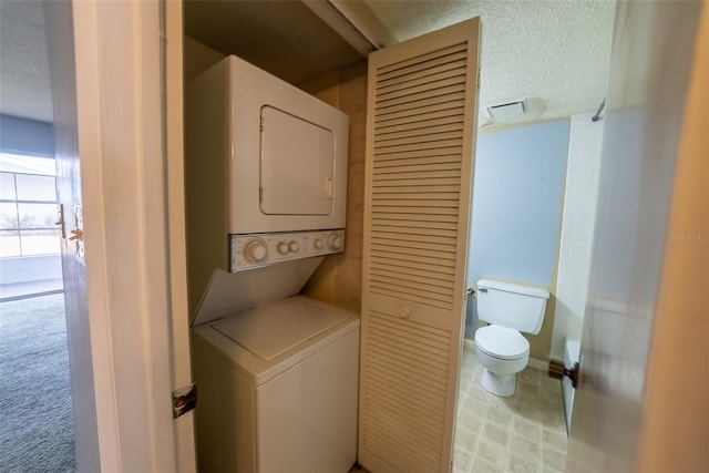 clothes washing area with stacked washer / drying machine and a textured ceiling