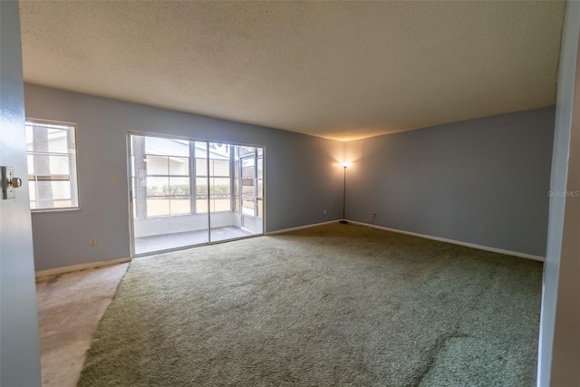 empty room with carpet flooring, a textured ceiling, and baseboards