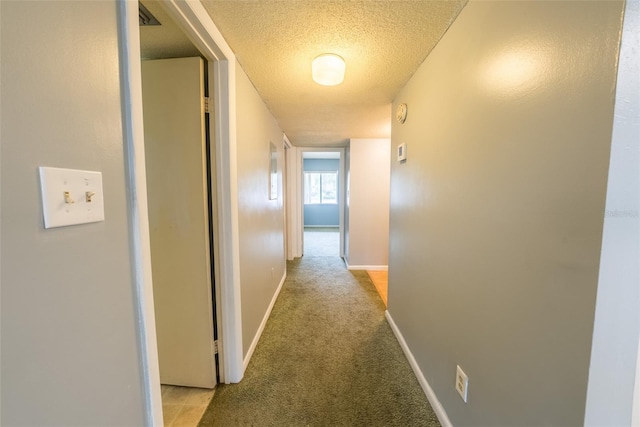 corridor with a textured ceiling, baseboards, and light colored carpet