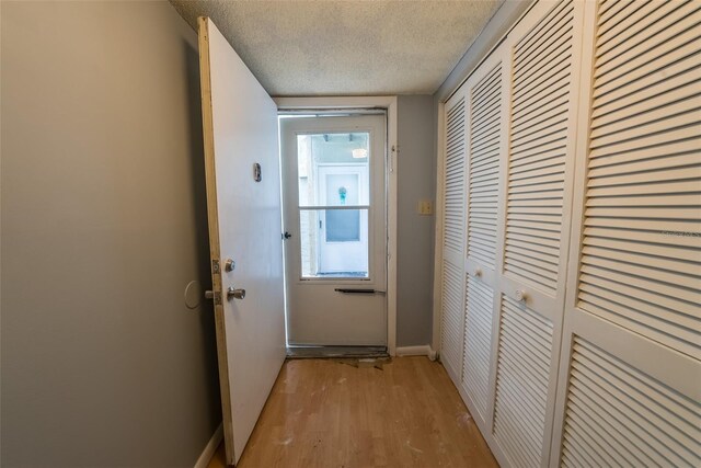 doorway with a textured ceiling, light wood-style floors, and baseboards