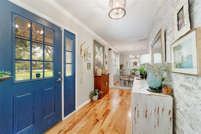 foyer entrance with a chandelier, light wood-type flooring, plenty of natural light, ornamental molding, and baseboards