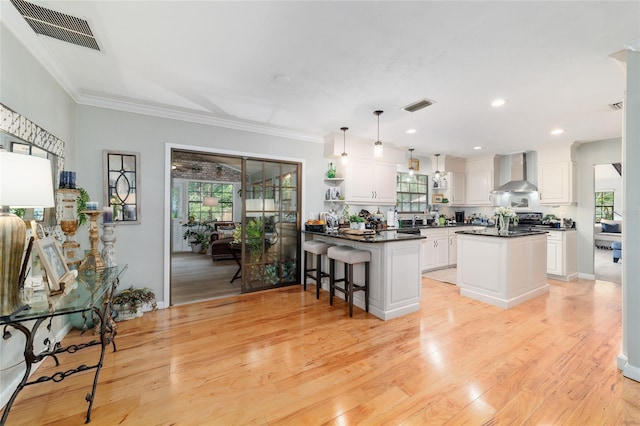 kitchen featuring wall chimney range hood, dark countertops, light wood-type flooring, white cabinetry, and crown molding
