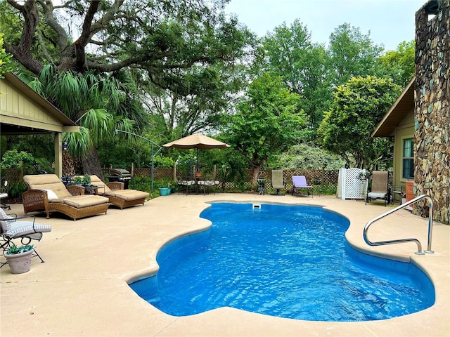 view of swimming pool featuring a patio area, fence, and view of wooded area