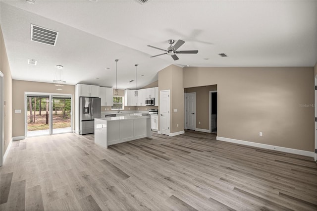 kitchen featuring stainless steel appliances, open floor plan, white cabinets, vaulted ceiling, and a ceiling fan