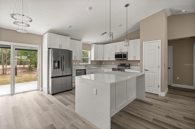 kitchen featuring appliances with stainless steel finishes, white cabinetry, a center island, vaulted ceiling, and baseboards