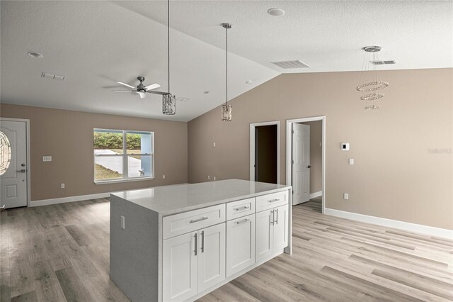 kitchen featuring vaulted ceiling, open floor plan, white cabinetry, light wood finished floors, and a textured ceiling