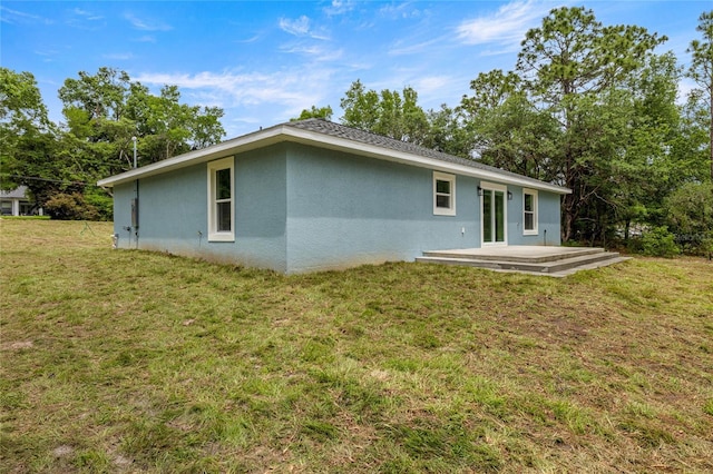 back of property with stucco siding and a yard