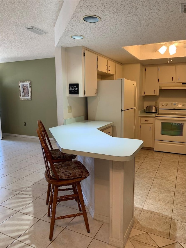 kitchen with white appliances, cream cabinets, a textured ceiling, and light tile patterned floors