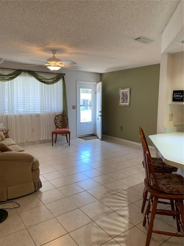 living room with light tile patterned flooring, a textured ceiling, ceiling fan, and baseboards