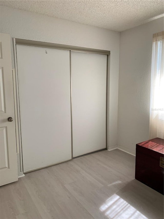 unfurnished bedroom with light wood-style floors, a closet, and a textured ceiling