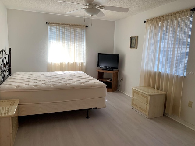 bedroom featuring light wood finished floors, baseboards, a textured ceiling, and a ceiling fan