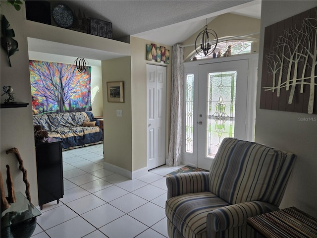 foyer with a chandelier, light tile patterned floors, vaulted ceiling, and baseboards