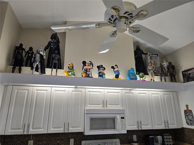 kitchen view of white microwave, a ceiling fan, range, and white cabinetry