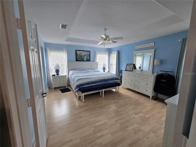 bedroom featuring a tray ceiling, light wood-style flooring, and a ceiling fan