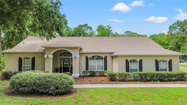 view of front of home featuring stucco siding, a front lawn, and a shingled roof