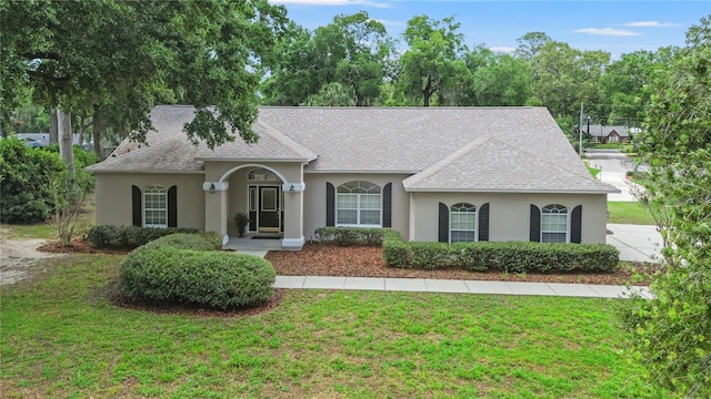 view of front of home featuring stucco siding, a shingled roof, and a front lawn