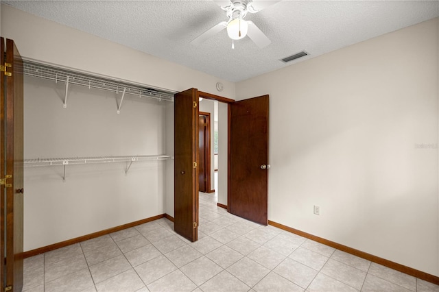 unfurnished bedroom featuring a textured ceiling, a closet, ceiling fan, baseboards, and light tile patterned floors