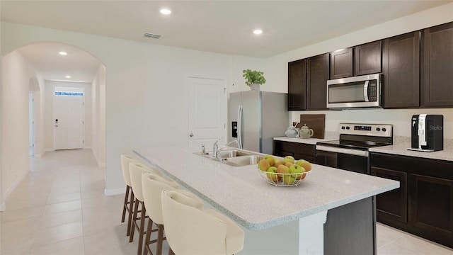 kitchen featuring appliances with stainless steel finishes, a sink, arched walkways, an island with sink, and a breakfast bar area