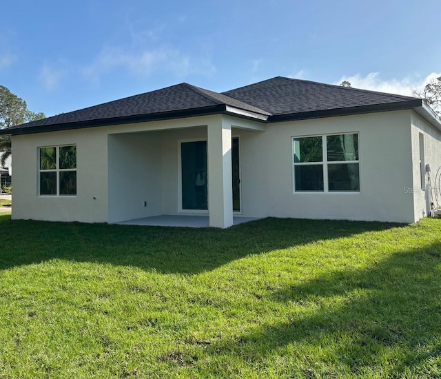 rear view of property with stucco siding, a lawn, a shingled roof, and a patio area