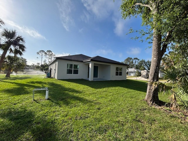 rear view of house with stucco siding and a yard