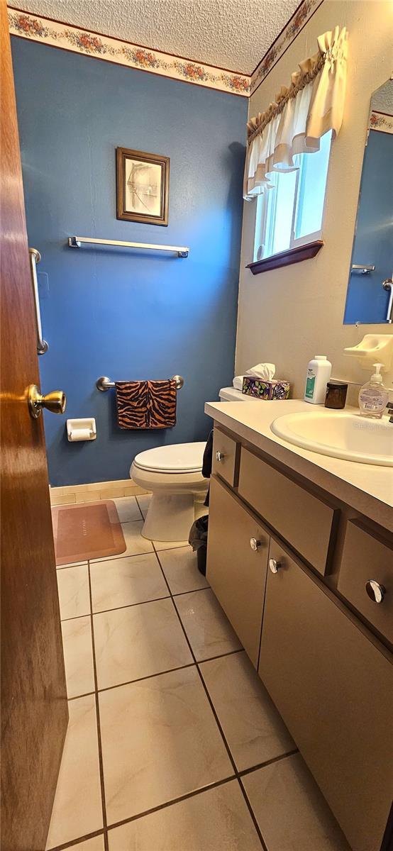 half bathroom featuring toilet, vanity, tile patterned floors, and a textured ceiling