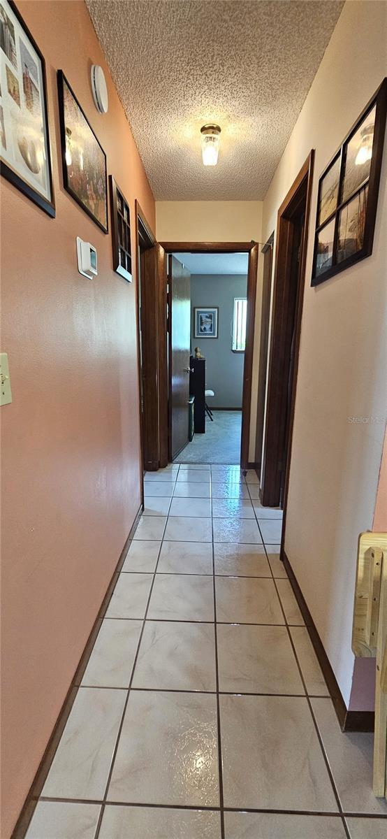 corridor with a textured ceiling, light tile patterned floors, and baseboards