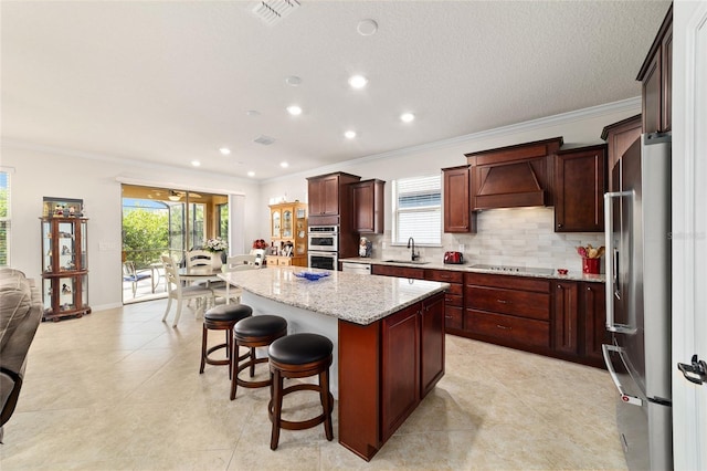 kitchen featuring stainless steel appliances, a sink, custom range hood, ornamental molding, and a kitchen island