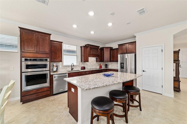 kitchen with stainless steel appliances, a center island, a sink, ornamental molding, and light stone counters