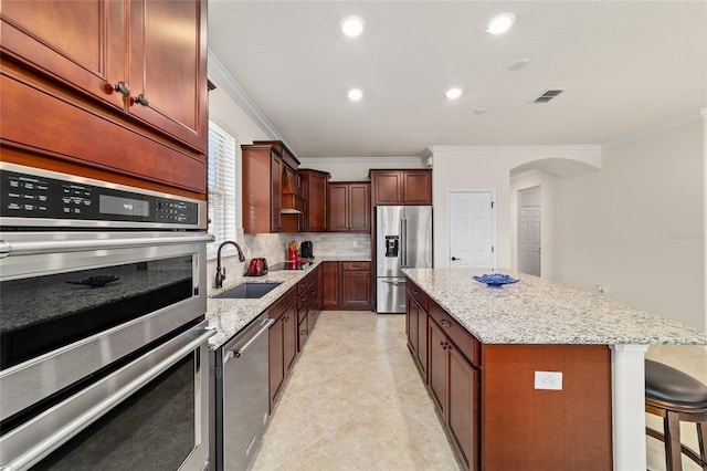 kitchen featuring stainless steel appliances, a sink, crown molding, tasteful backsplash, and a center island
