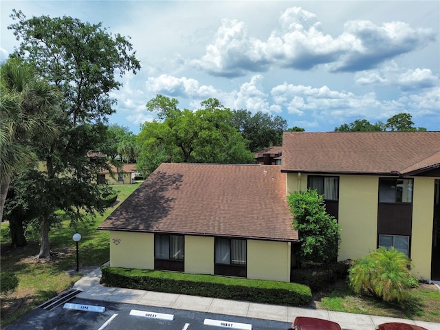 view of front of property with uncovered parking, stucco siding, and roof with shingles