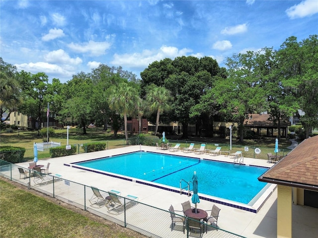 community pool with fence, a patio, and view of scattered trees