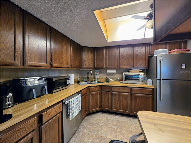 kitchen with appliances with stainless steel finishes, a sink, a ceiling fan, and butcher block countertops