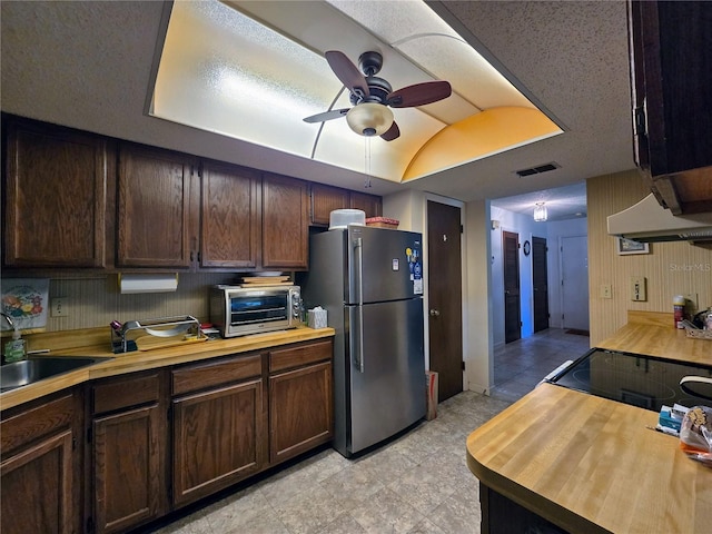 kitchen featuring freestanding refrigerator, wooden counters, a ceiling fan, a sink, and dark brown cabinetry