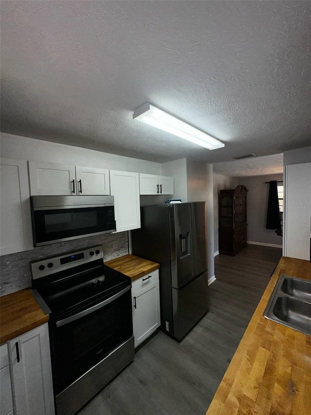 kitchen featuring wood counters, appliances with stainless steel finishes, a sink, white cabinetry, and dark wood-type flooring