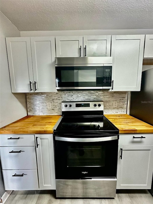 kitchen featuring stainless steel microwave, butcher block countertops, electric range oven, light wood-type flooring, and decorative backsplash