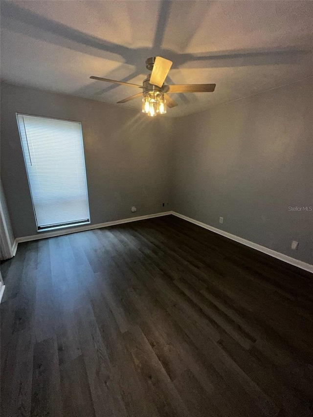 empty room featuring dark wood-style flooring, a ceiling fan, and baseboards