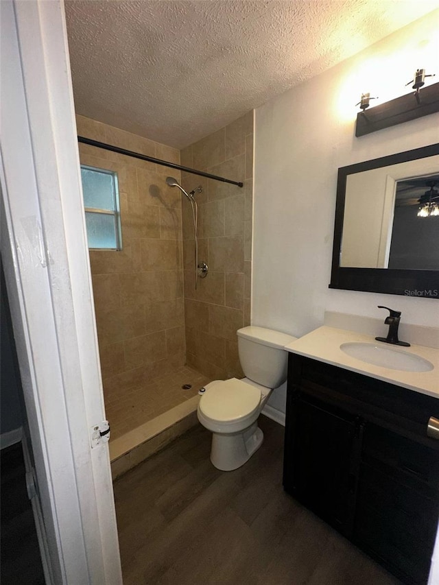 bathroom with wood finished floors, a textured ceiling, vanity, tiled shower, and toilet