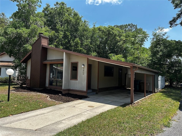 view of front of house featuring driveway, a chimney, an attached carport, and a front yard
