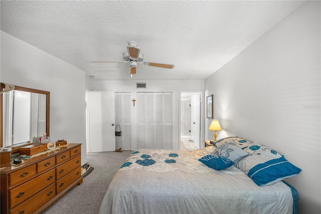 bedroom featuring light carpet, two closets, a textured ceiling, and ceiling fan